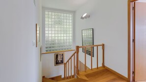 Una escalera con barandas y piso de madera, que conduce a una habitación con un ventanal grande y cuadros enmarcados en la pared.