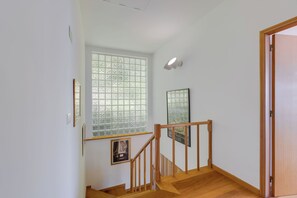 Una escalera con barandas y piso de madera, que conduce a una habitación con un ventanal grande y cuadros enmarcados en la pared.
