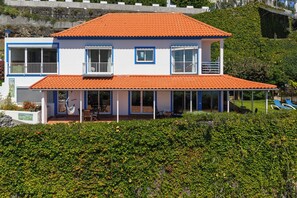 A two-story house with a red-tiled roof, white walls with blue trim, and a balcony. - Sea Sky House By Holiday Rental Madeira (Ribeira Brava)