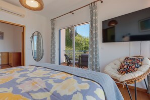 A bedroom with a bed, a TV, a chair, and a balcony with a view. - Sea Sky House By Holiday Rental Madeira (Ribeira Brava)