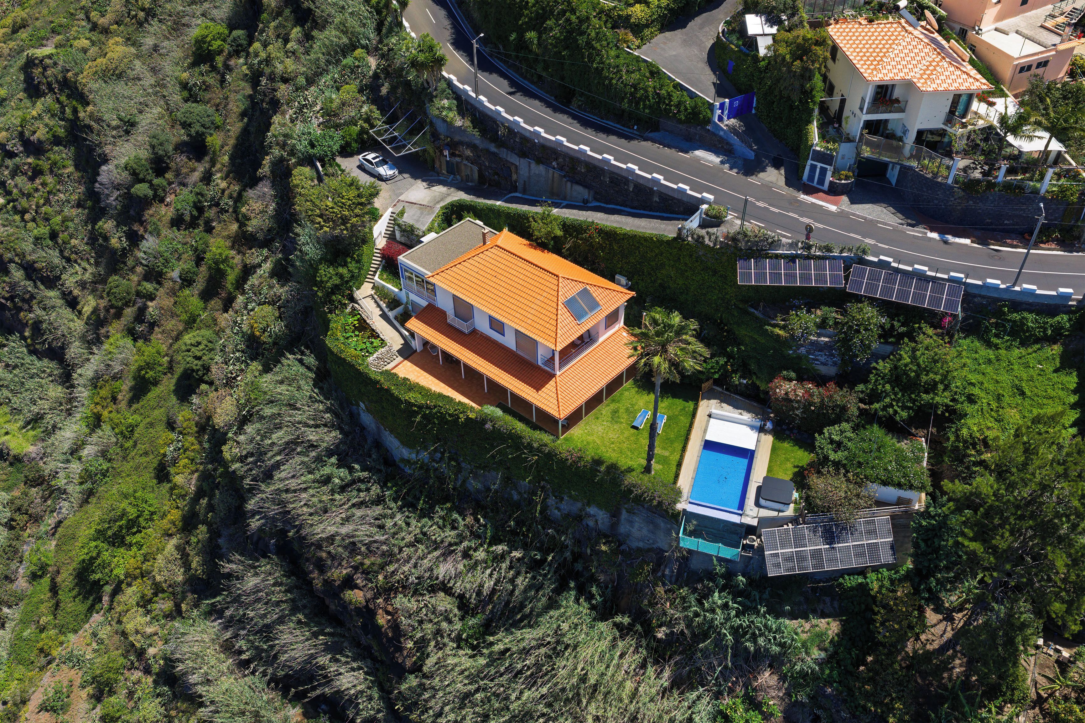 Vue aérienne d’une maison dotée d’une piscine, de panneaux solaires et d’une route sinueuse à proximité.