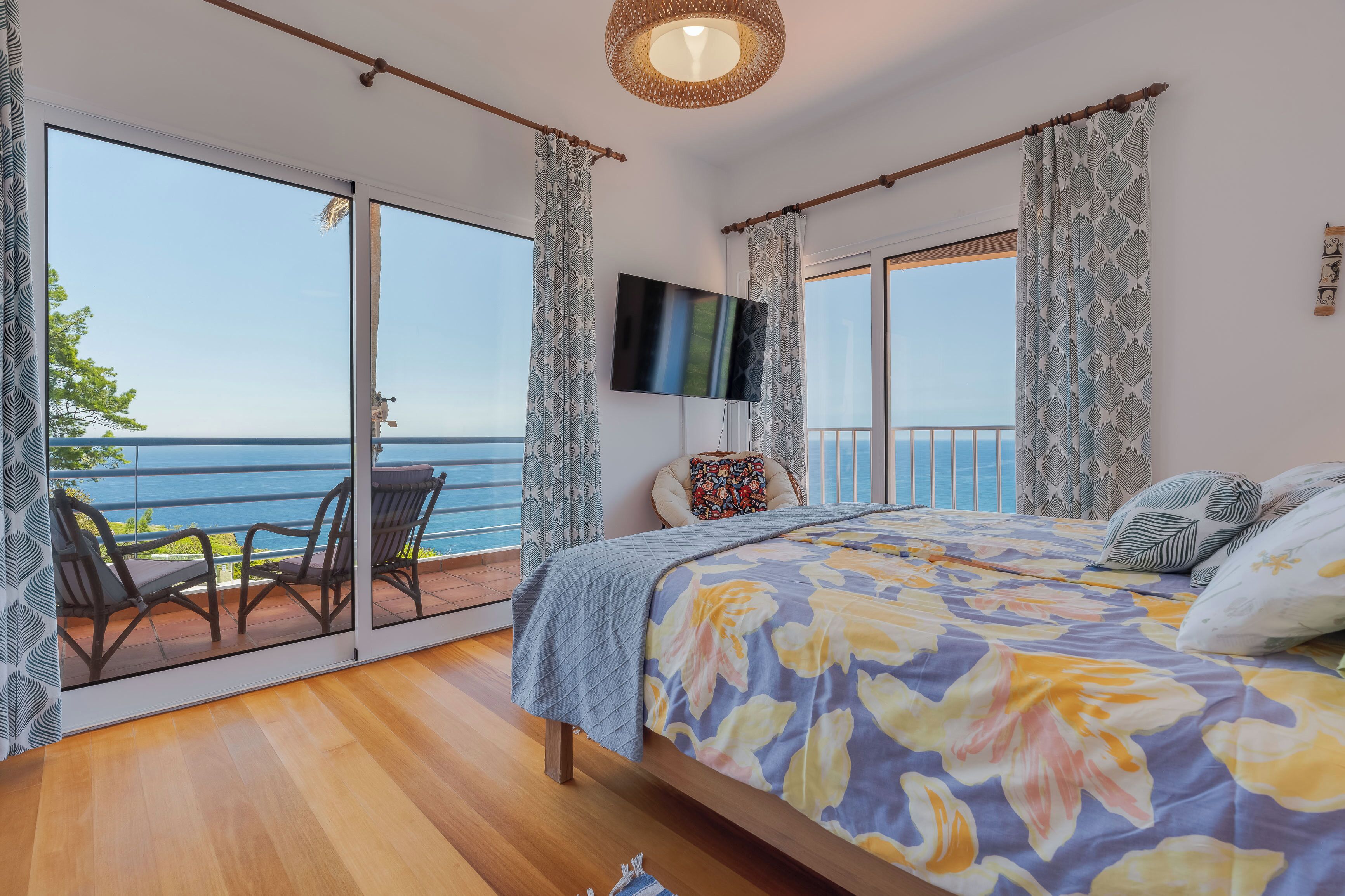 A bedroom with a large bed, a TV, and a balcony with a view of the sea.