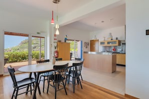 Une cuisine moderne avec des meubles en bois, un coin repas comprenant une table et des chaises, et une vue sur une colline.