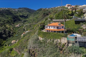 Une propriété située sur une colline, avec une maison dotée d’un toit rouge, d’une piscine et de panneaux solaires.