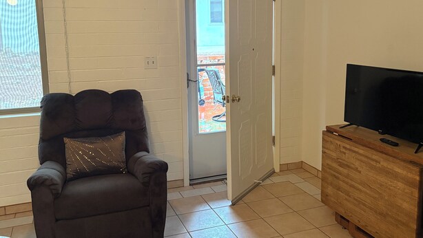 Un salon avec un canapé en cuir foncé, un meuble TV en bois et une porte donnant sur un espace extérieur.