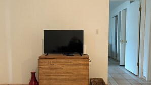 Un meuble en bois pour la télévision, sur lequel est posée une télévision à écran plat, un vase rouge et un panier en osier, dans un couloir.