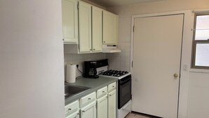 Une cuisine de taille réduite avec des meubles de couleur vert clair, une cuisinière à gaz, une machine à café et un évier.