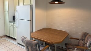Une cuisine de taille réduite, avec un réfrigérateur blanc, une table en bois et deux chaises à motifs.
