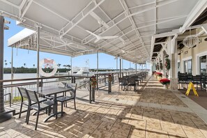 An outdoor terrace with tables and chairs, overlooking a body of water and a marina. - ~NEW~ NSB Coastal Executive Retreat. Close To Beach/Flagler/Canal + Pool/Hot tub (New Smyrna Beach)