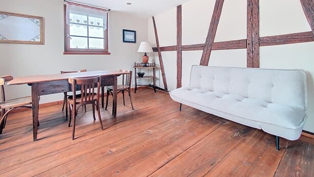 A room with a wooden dining table, chairs, a white sofa, and exposed wooden beams on the ceiling. - La Perle du Ried N° 7 near Europapark - Typical Alsatian dovecotes (Boofzheim)