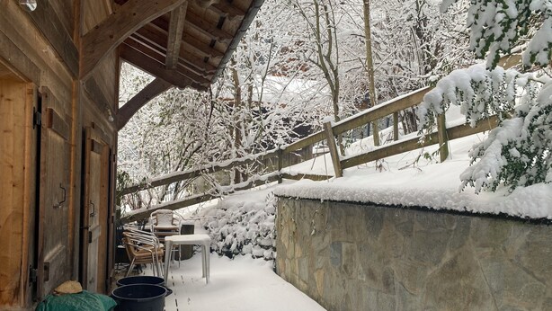 Una terraza de madera con mobiliario exterior y un muro de piedra.