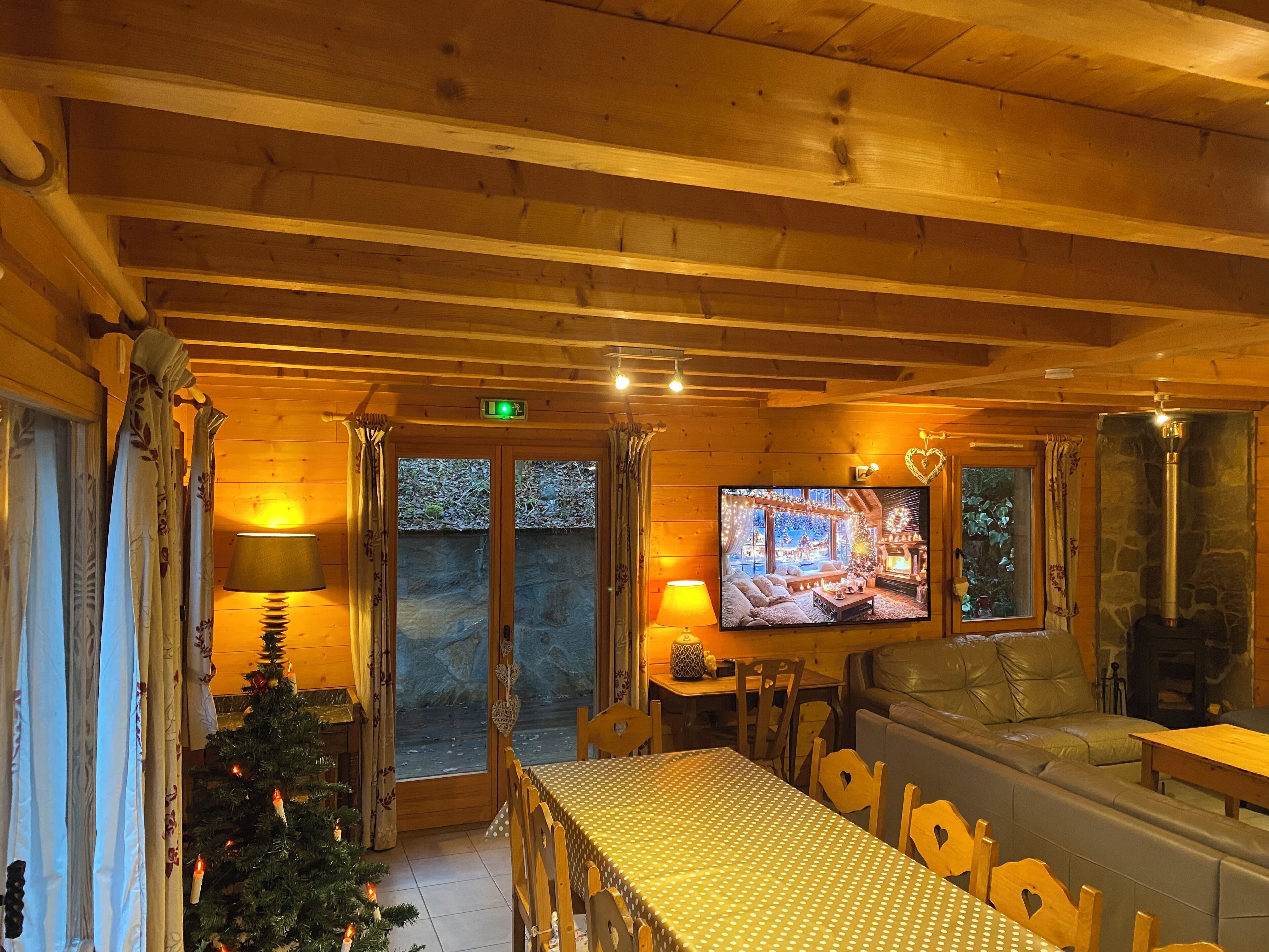 A cozy wooden cabin interior with a television, a fireplace, a sofa, and a dining table.