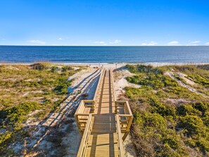 A wooden boardwalk leading to the beach with sand dunes and vegetation on either side. - Serenity Now: Spacious 4BR Beach House in Caswell Beach, Oak Island (Oak Island)