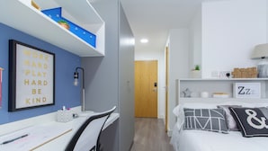 Une chambre à coucher moderne avec un bureau, un lit agrémenté de coussins décoratifs, une étagère murale avec une plante en pot et une citation inspirante sur le mur.