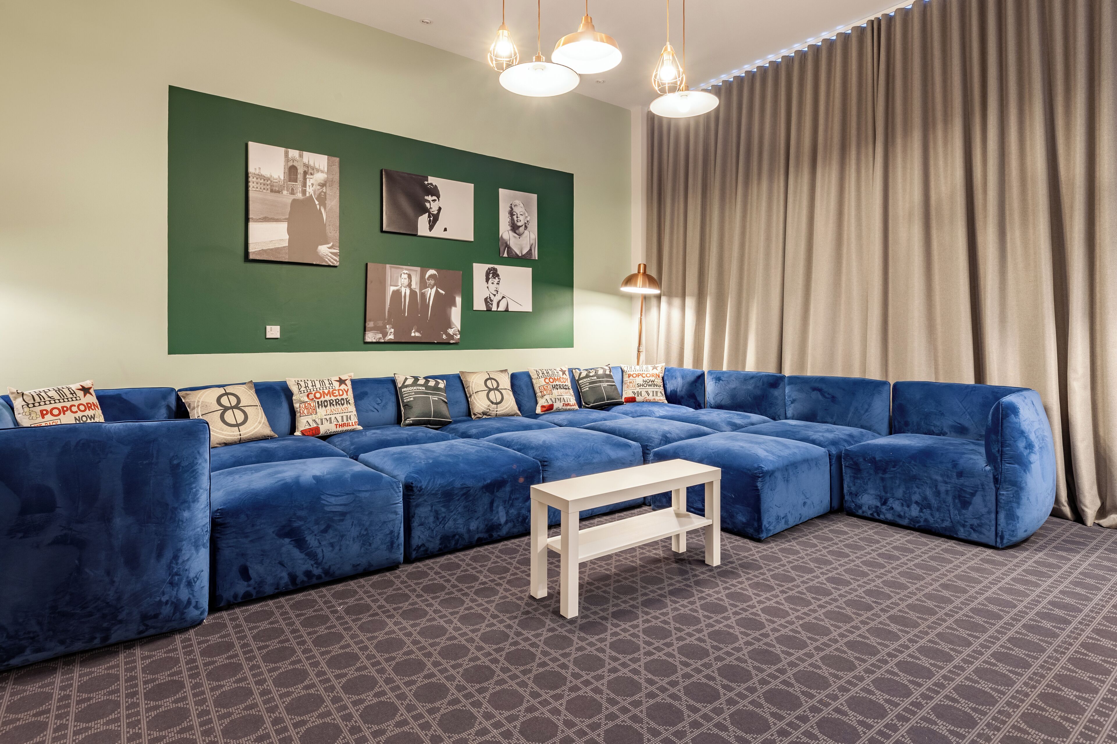 Uma sala de estar moderna com um sofá seccional azul, uma mesinha de centro branca e uma parede verde decorada com quadros.