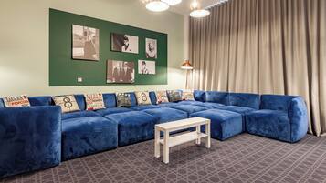 Uma sala de estar moderna com um sofá seccional azul, uma mesinha de centro branca e uma parede verde decorada com quadros.