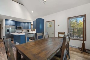 Une cuisine moderne avec des meubles bleus, un réfrigérateur en acier inoxydable et un coin repas comprenant une table et des chaises en bois.