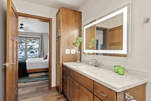 Une salle de bain avec un grand miroir, des meubles en bois, un comptoir en marbre et une bougie en verre vert.