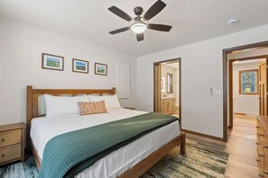Une chambre Ă coucher comprenant un lit, un ventilateur de plafond, une table de chevet, une commode et une porte donnant sur une autre piĂšce.