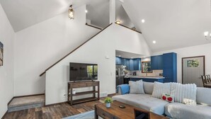 Un salon moderne comprenant un téléviseur, un canapé, une table basse et un escalier menant à la cuisine.