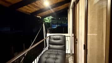 Un balcón con una zona de estar acolchada, vigas de madera en el techo y un ventanal de vidrio que da a un espacio interior.