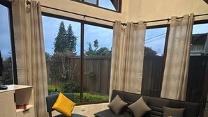 A spacious living area with a high ceiling, large windows, and a view of the outdoors. - Casa Viento - Private Pool, Garden & BBQ (San Pedro La Laguna)