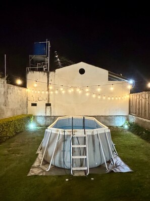 An outdoor swimming pool with a ladder, surrounded by a grassy area and a white building with string lights. - Casa Viento - Private Pool, Garden & BBQ (San Pedro La Laguna)