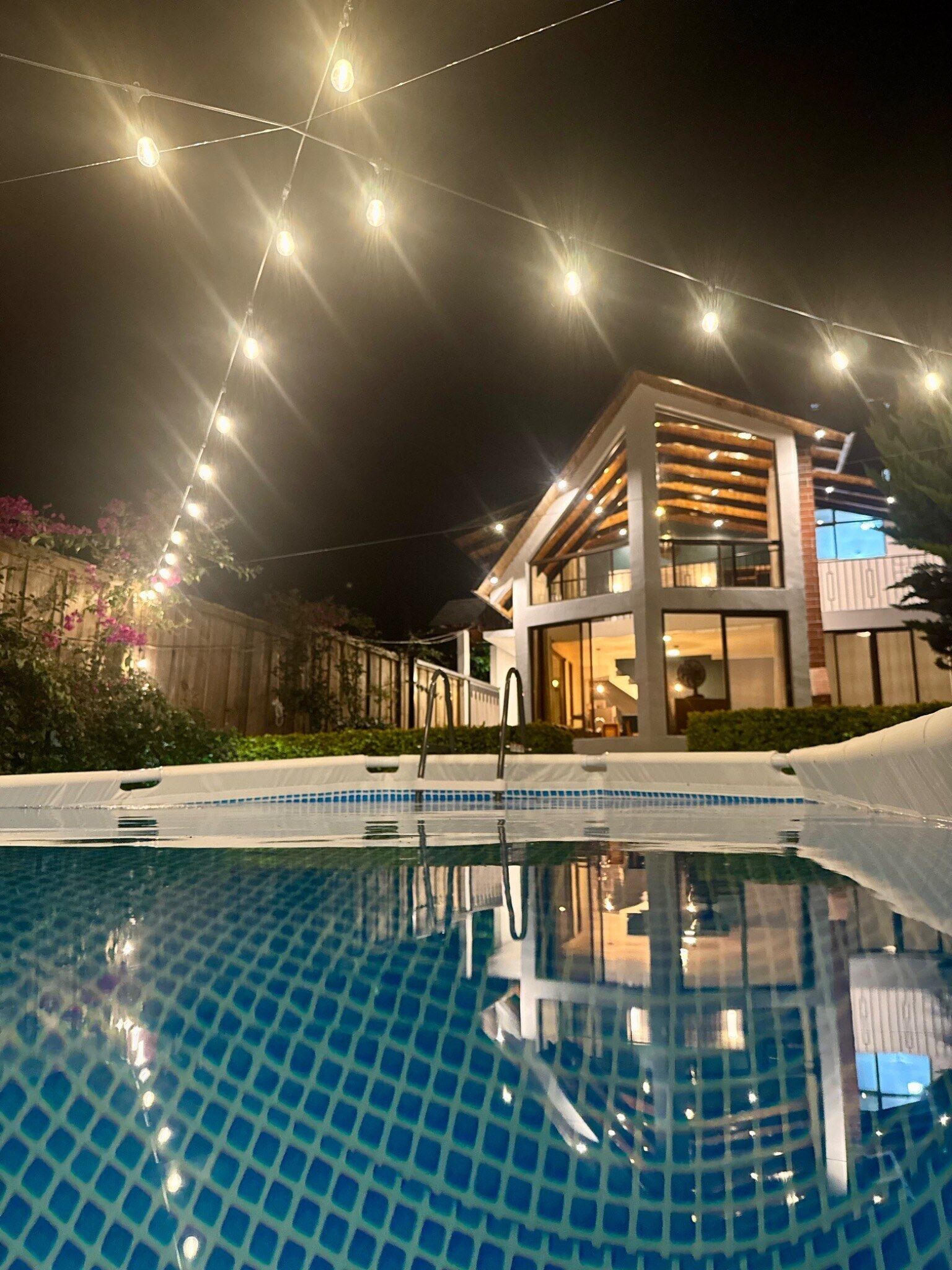 Une maison moderne dotée d’une piscine, de guirlandes lumineuses et d’une terrasse en bois.