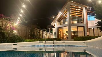 Une maison moderne dotée d’une piscine, de guirlandes lumineuses et d’une terrasse en bois.
