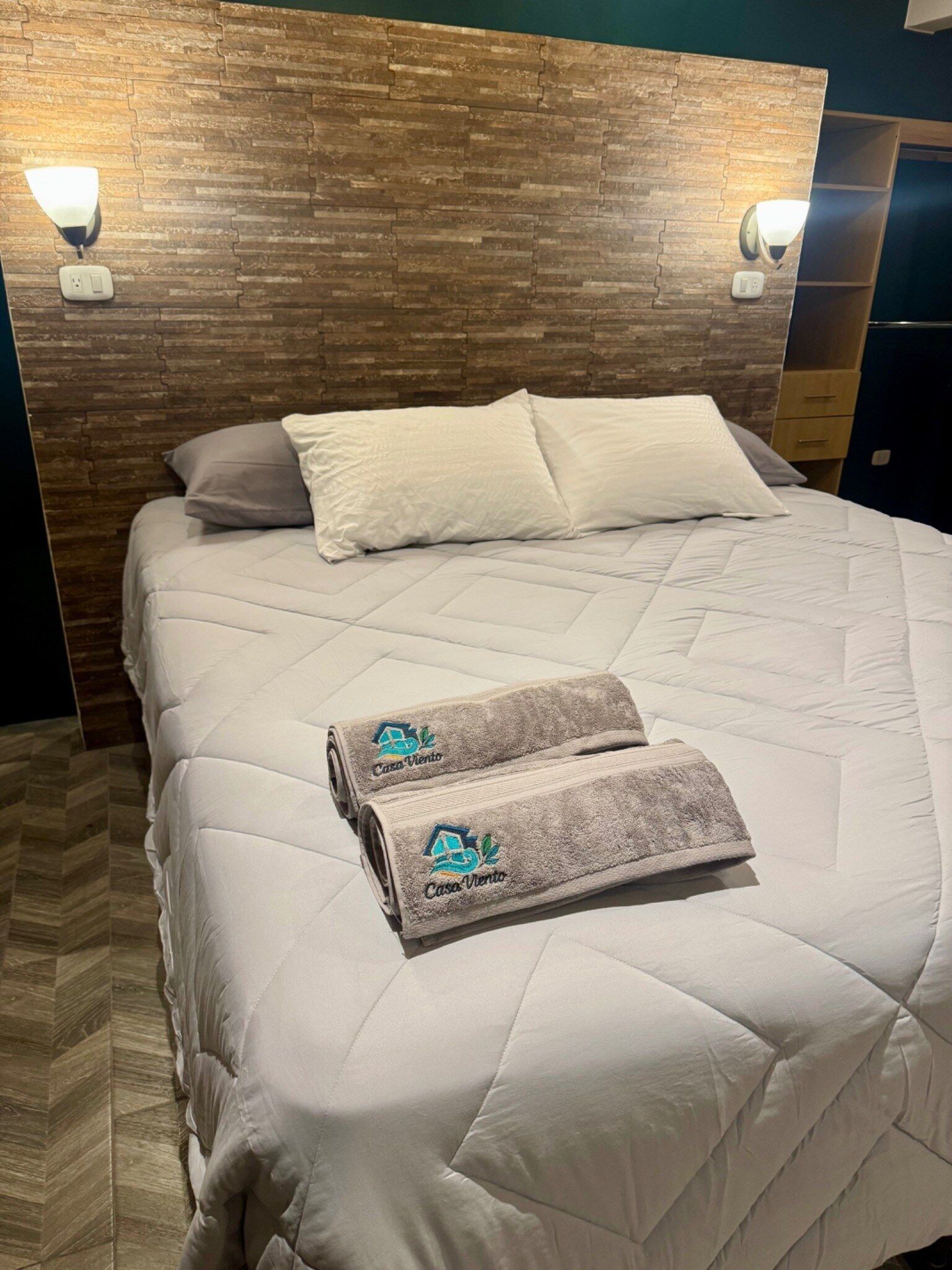 Un lit bien fait, avec une couette blanche matelassée, deux oreillers et deux serviettes ornées d’un logo.