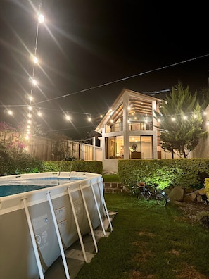 Une maison moderne à deux étages, dotée d’une piscine et illuminée de guirlandes lumineuses.