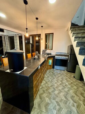 A modern kitchen with a central island, wooden cabinets, a built-in oven, and a herringbone-patterned floor. - Casa Viento - Private Pool, Garden & BBQ (San Pedro La Laguna)