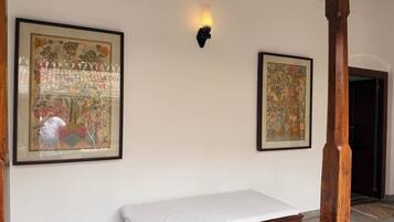 A room with a wooden bed, two framed artworks on the wall, and a wall-mounted light fixture.