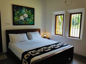 Ein Schlafzimmer mit einem Bett, einem Nachttisch, einem Wandbild und zwei vergitterten Fenstern.