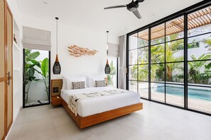 Ein modernes Schlafzimmer mit einem großen Bett, einem Deckenventilator und Blick auf einen Swimmingpool.