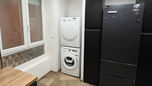 A compact kitchen with a washing machine, a refrigerator, and a window with blinds.