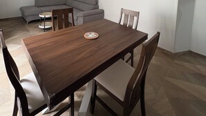 A dining area with a wooden table and four chairs, a gray sectional sofa, and a small round table with a board game.
