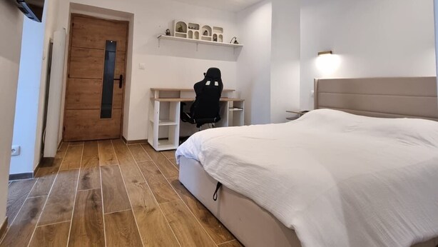 A modern bedroom with a large bed, a desk with shelves, and a gaming chair.