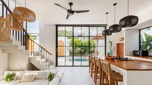 A modern kitchen with a wooden island, bar stools, and a dining area. - Family Nest 2BR Villa with pool and balcony (Kabupaten Badung)
