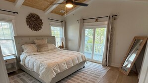 Ein Schlafzimmer mit Bett, Deckenventilator, großem Spiegel und Blick ins Freie.