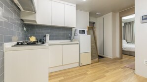 A compact kitchen with white cabinets, a microwave, and a gas stove. - Anne House (Seoul)