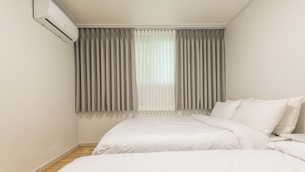 A bedroom with two beds, a window with curtains, and an air conditioning unit. - Anne House (Seoul)