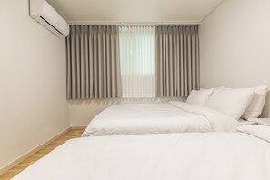 Une chambre avec deux lits, une fenêtre avec des rideaux et un appareil de climatisation.