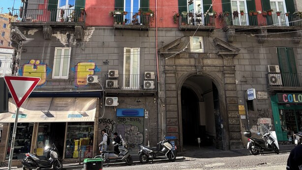 Un immeuble à plusieurs étages, doté de balcons, d’une devanture de magasin et de scooters garés.