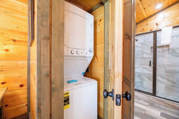 A compact room with a white washing machine, a wooden door, and a glass shower area.
