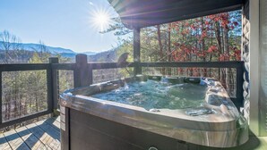 Un jacuzzi en una terraza de madera con vista a árboles y montañas.