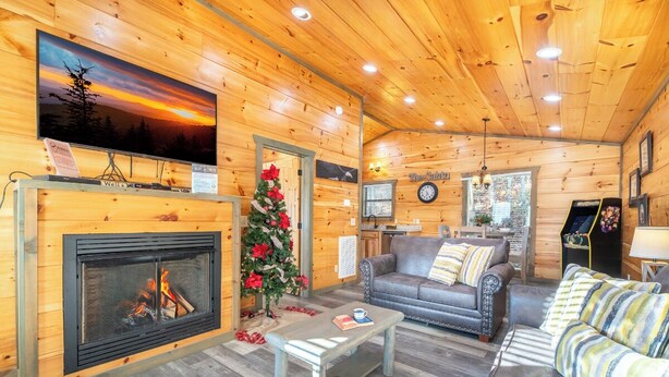 Un interior de cabaña acogedor con chimenea, un árbol de Navidad, un sofá y un televisor.