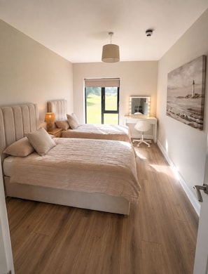 A bedroom with two beds, a desk with a mirror, and a painting of a lighthouse. - Sea Mourne View - Cozy Irish Retreat with Sea Breezes & Mountain Views (Carlingford)