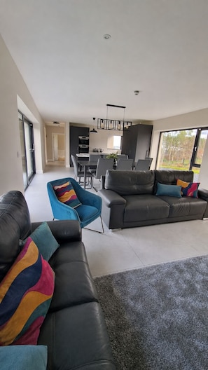 A modern living room with a sofa, chairs, and a dining area with a table and chairs. - Sea Mourne View - Cozy Irish Retreat with Sea Breezes & Mountain Views (Carlingford)