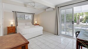 A bedroom with a bed, two bedside tables with lamps, a ceiling fan, and a sliding glass door leading to an outdoor area. - Fantastic beach house tucked away in paradise (Amity)